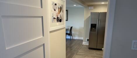 A hallway with a wooden floor, white walls, and a stainless steel refrigerator.