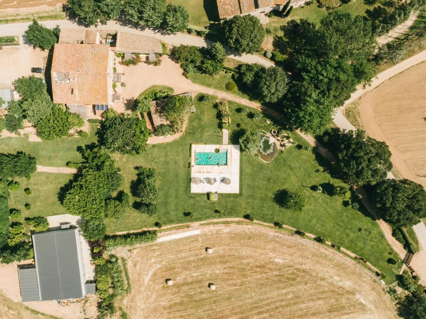 Vista aérea de una propiedad con piscina, follaje circundante y un campo amplio.