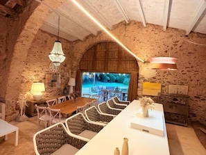 Un intérieur rustique avec des murs en pierre, une table à manger en bois, des sièges rembourrés et des luminaires suspendus.