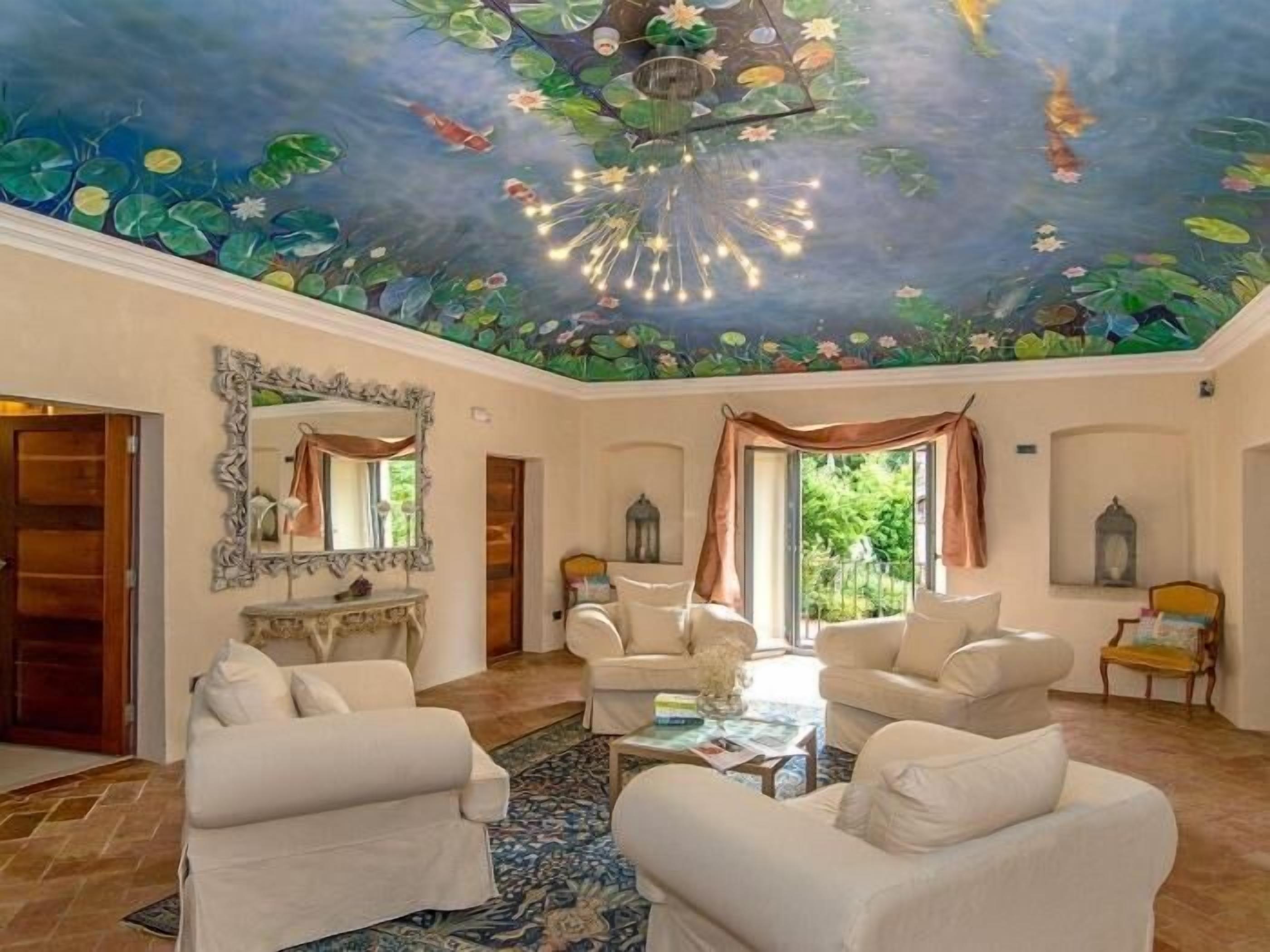 Ein geräumiges Wohnzimmer mit weißen Sofas, einem gemusterten Teppich und einer Deckenmalerei von Seerosen und Fischen.