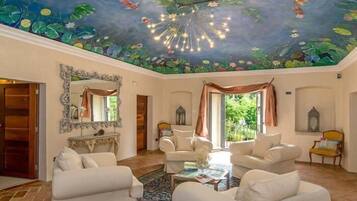 Ein geräumiges Wohnzimmer mit weißen Sofas, einem gemusterten Teppich und einer Deckenmalerei von Seerosen und Fischen.