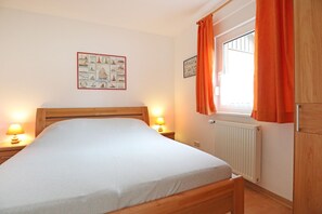 Une chambre à coucher avec un lit en bois, deux lampes de chevet, une fenêtre avec des rideaux orange et un tableau accroché au mur.
