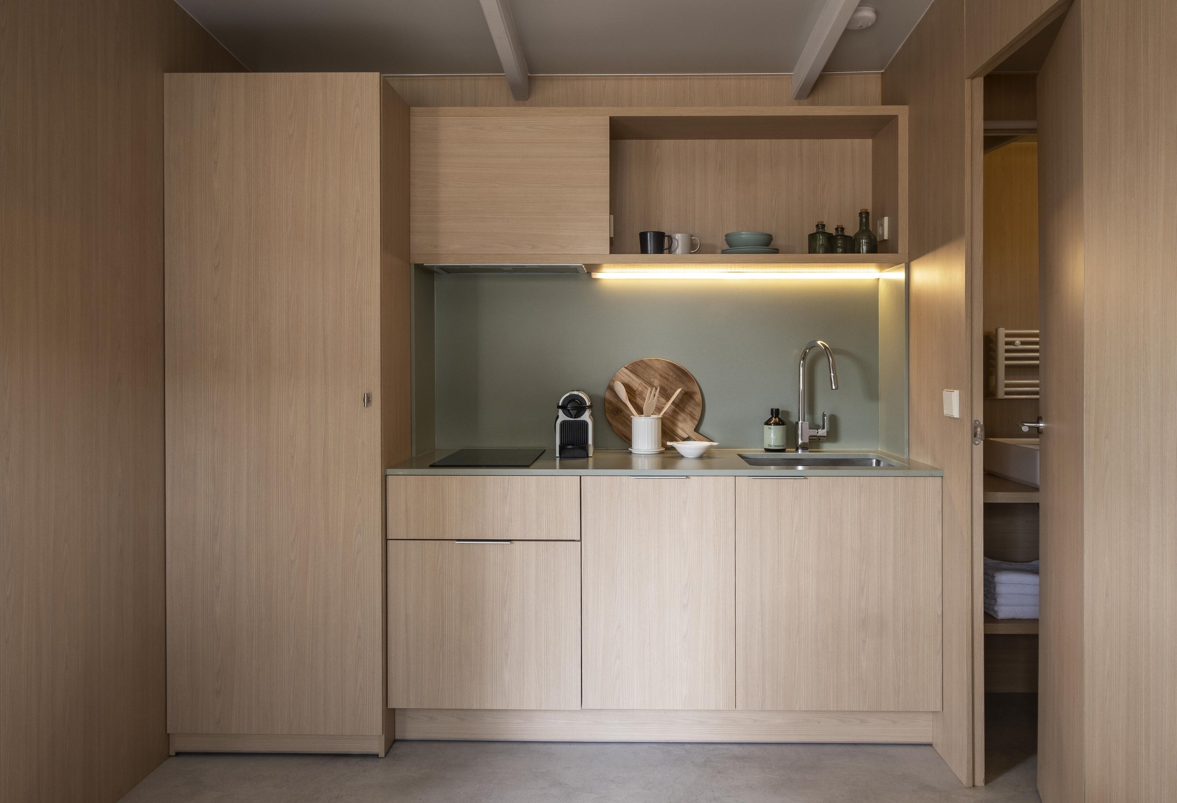 A compact kitchen with wooden cabinets, a countertop, a sink, and a built-in shelf with kitchenware.