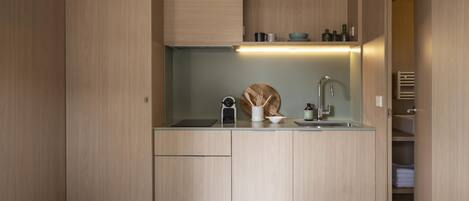 Une cuisine compacte avec des meubles en bois, un plan de travail, un évier et une étagère intégrée où sont rangés les ustensiles de cuisine.