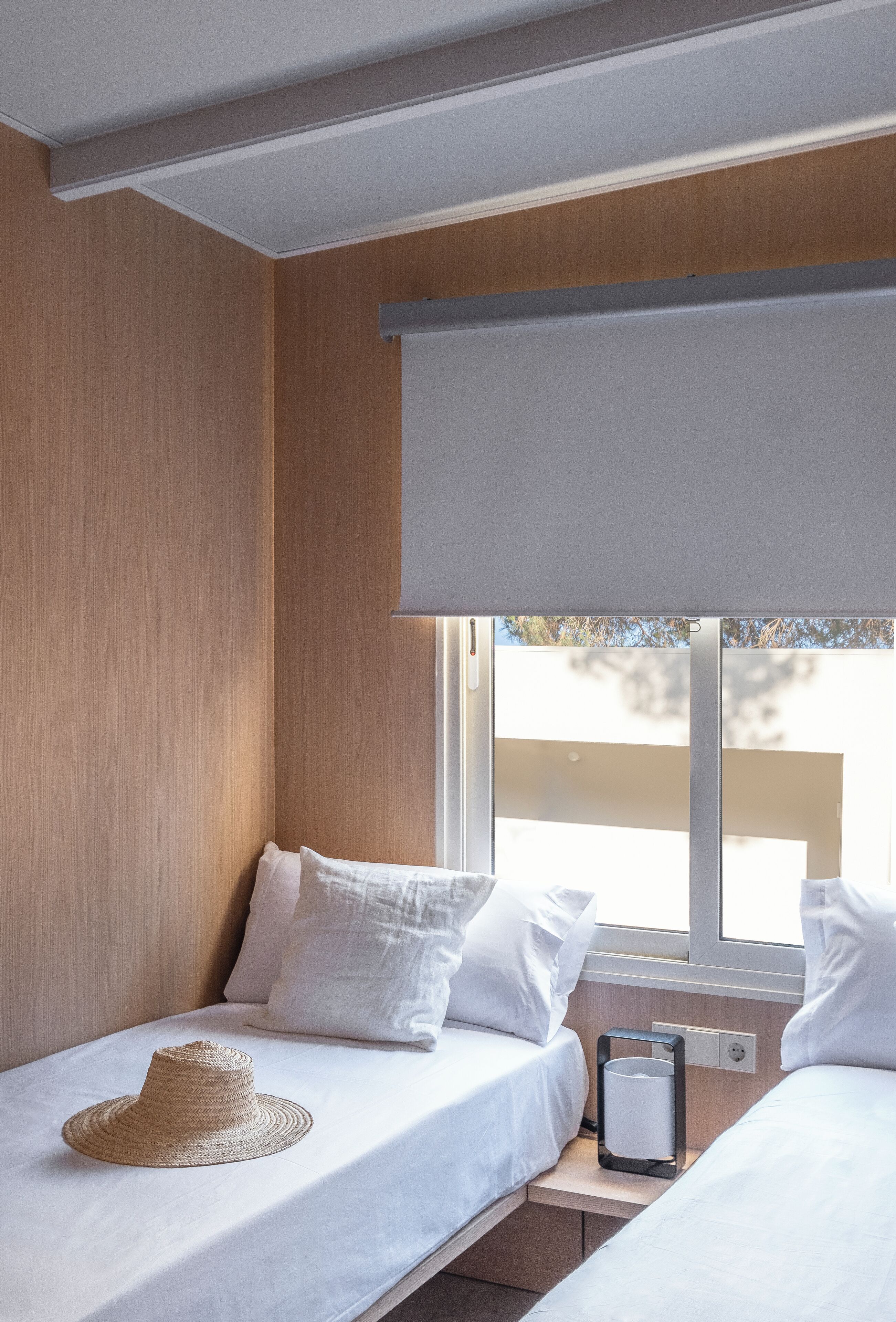 Een kamer met twee bedden, een raam met uitzicht en een strohoed op een van de bedden.