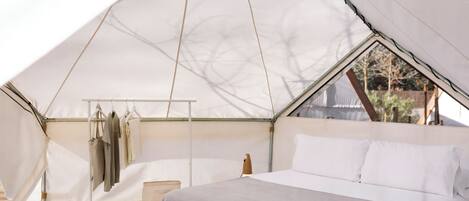 A tented accommodation with a bed, hanging clothes rack, and a small table.