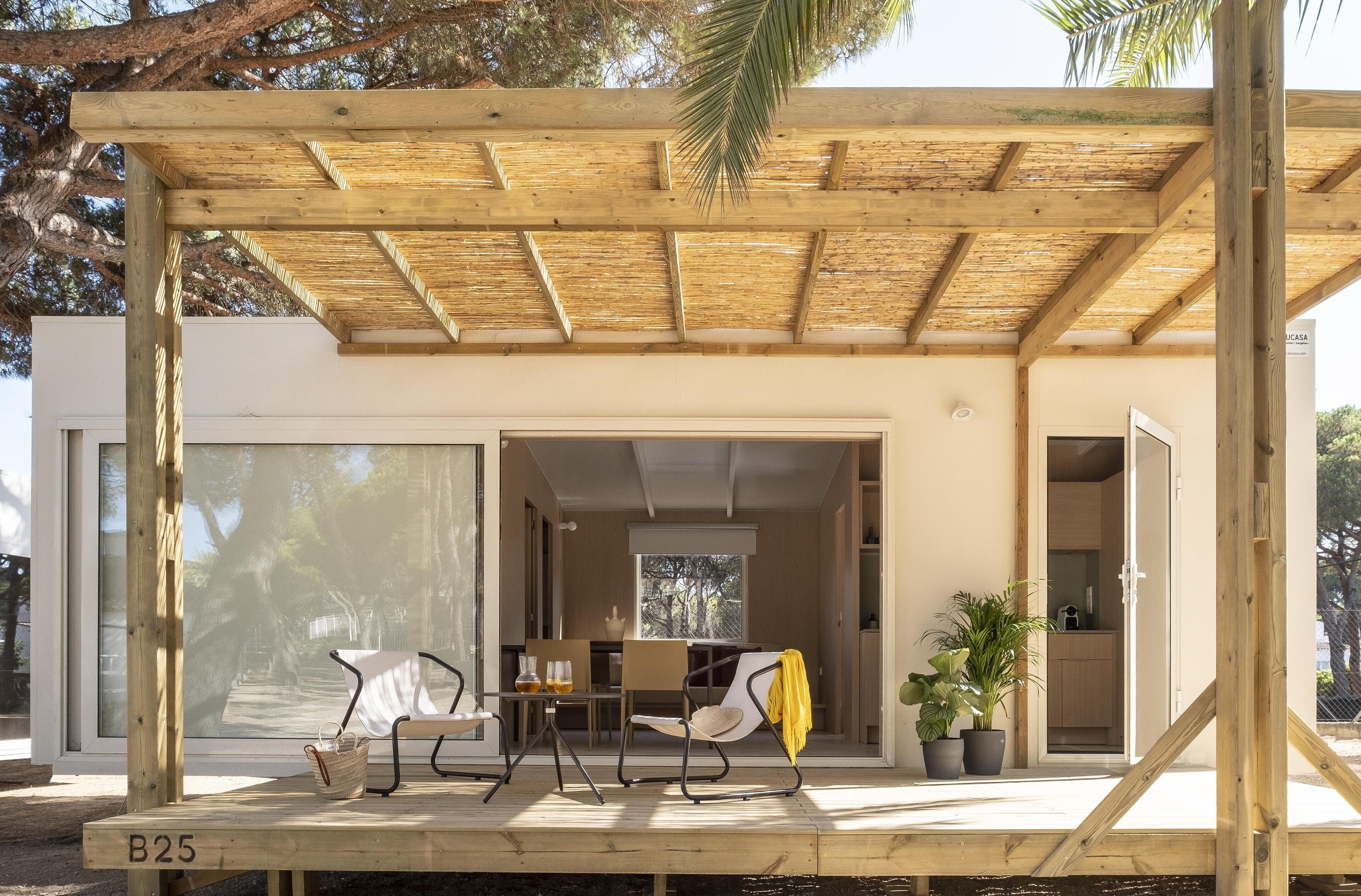 Un'area relax esterna moderna con un gazebo in legno, un tavolo, sedie e una pianta in vaso.