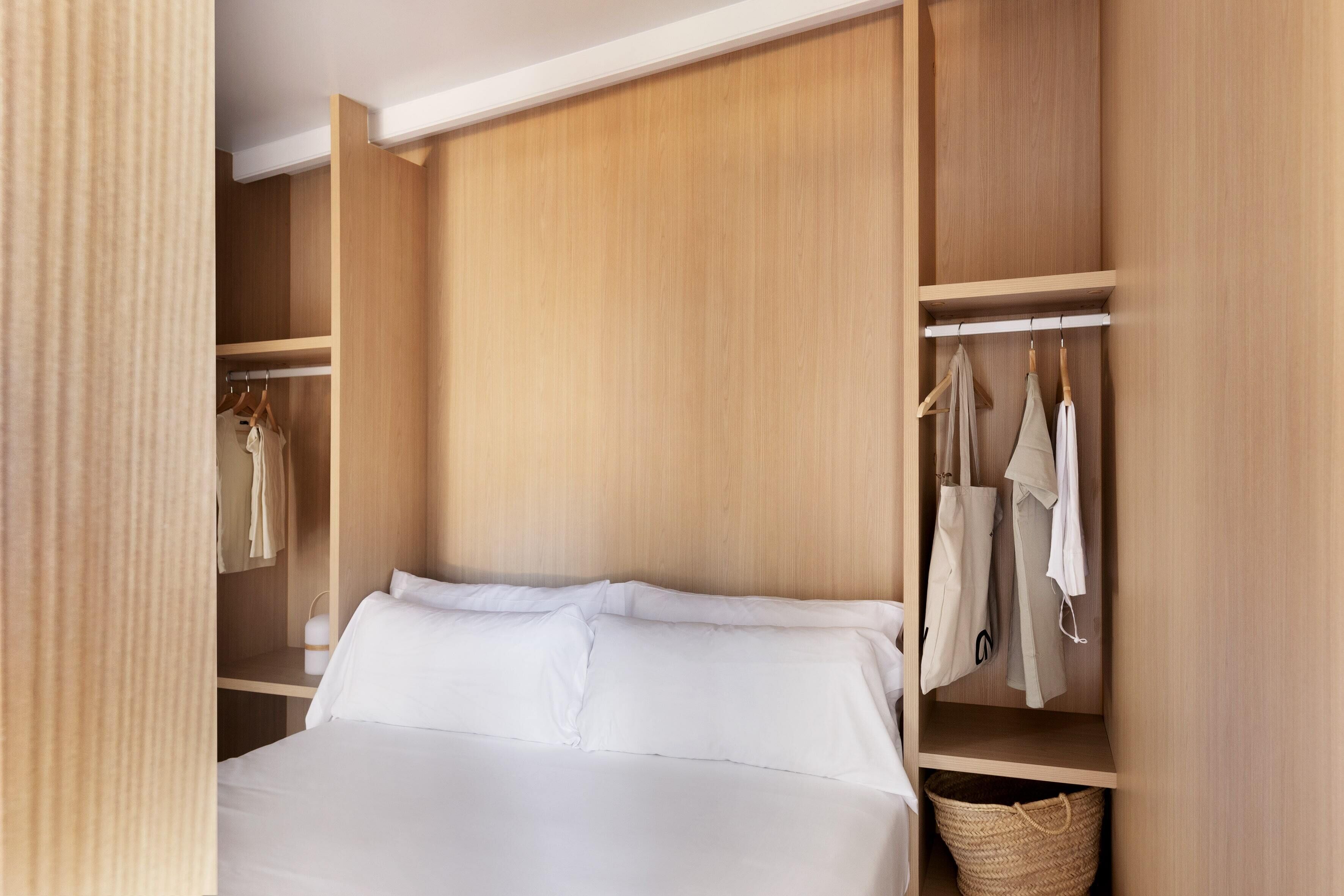 Une chambre à coucher avec un lit, une armoire en bois et des vêtements suspendus.