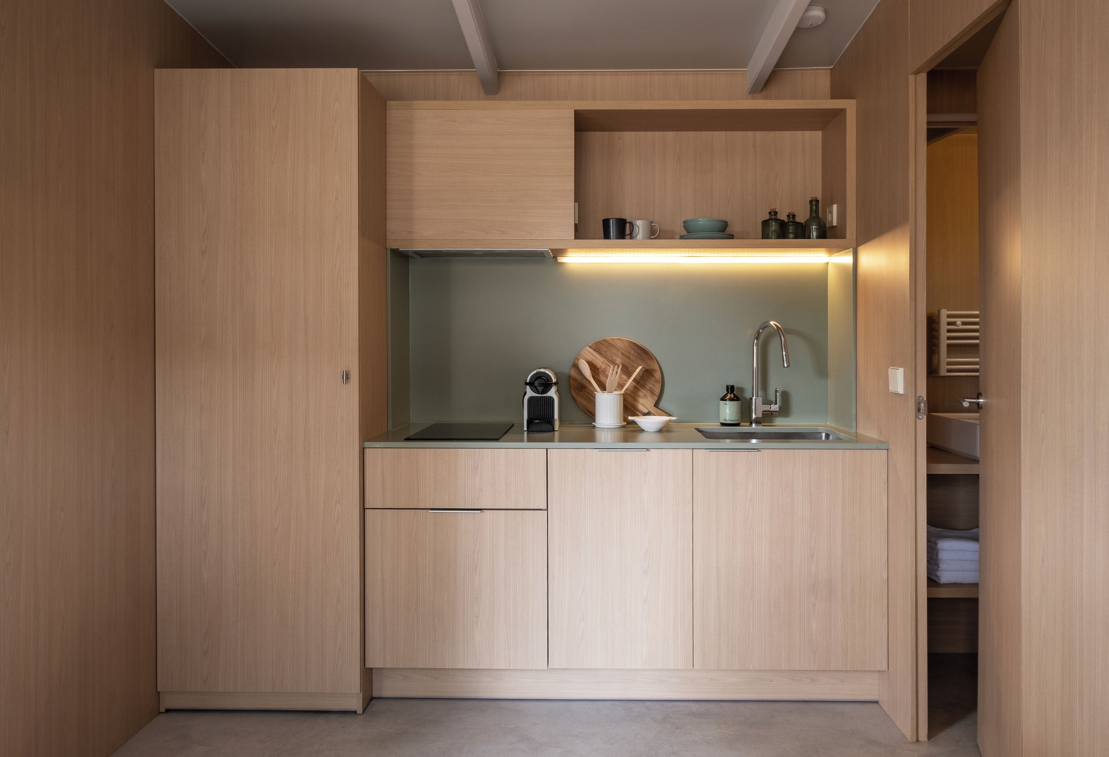 A compact kitchen with wooden cabinetry, a built-in sink, and a countertop with a kettle and a bottle.