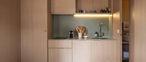 A compact kitchen with wooden cabinetry, a built-in sink, and a countertop with a kettle and a bottle.