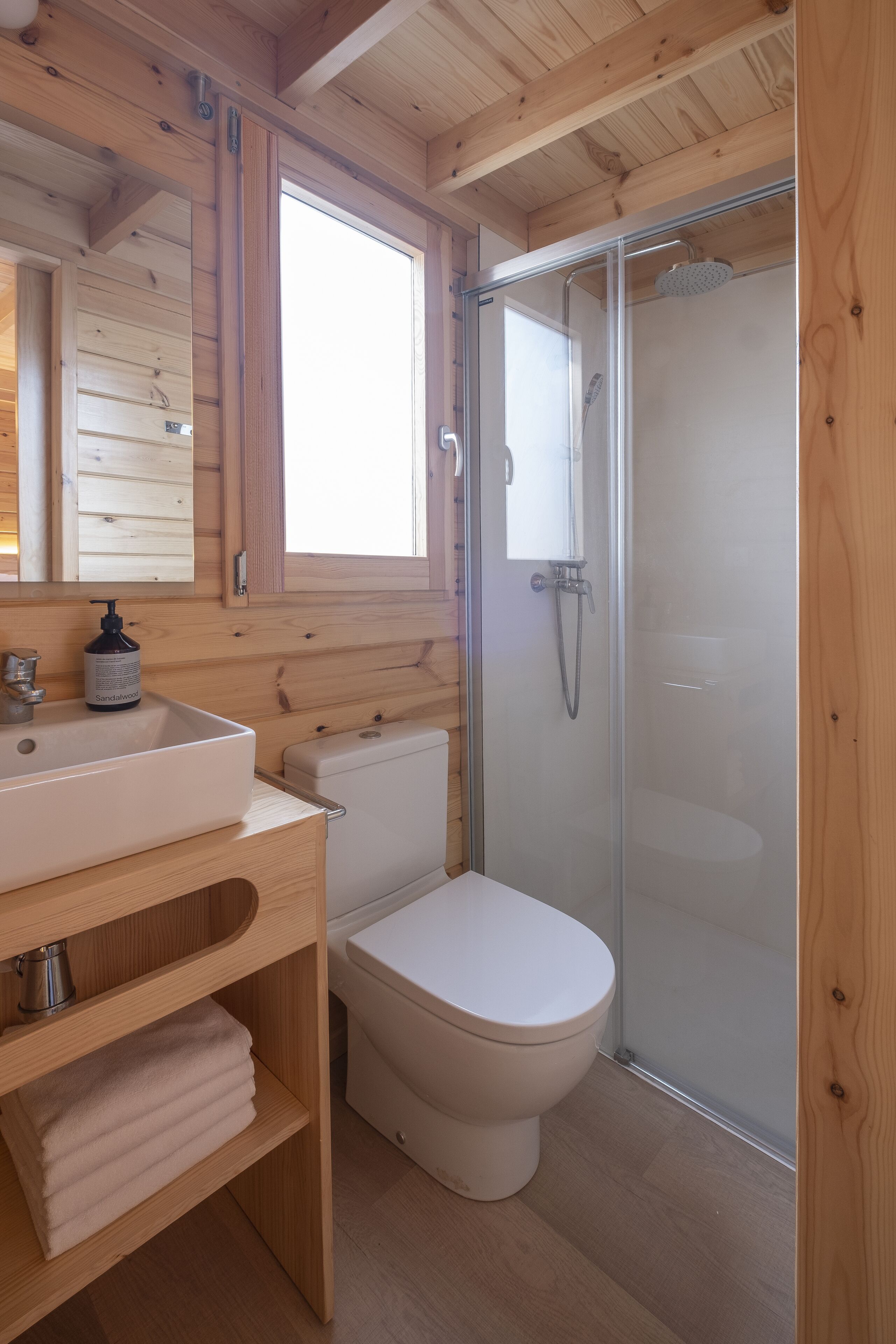 Baño de cabaña de madera con lavabo, inodoro y mampara de vidrio para la ducha.