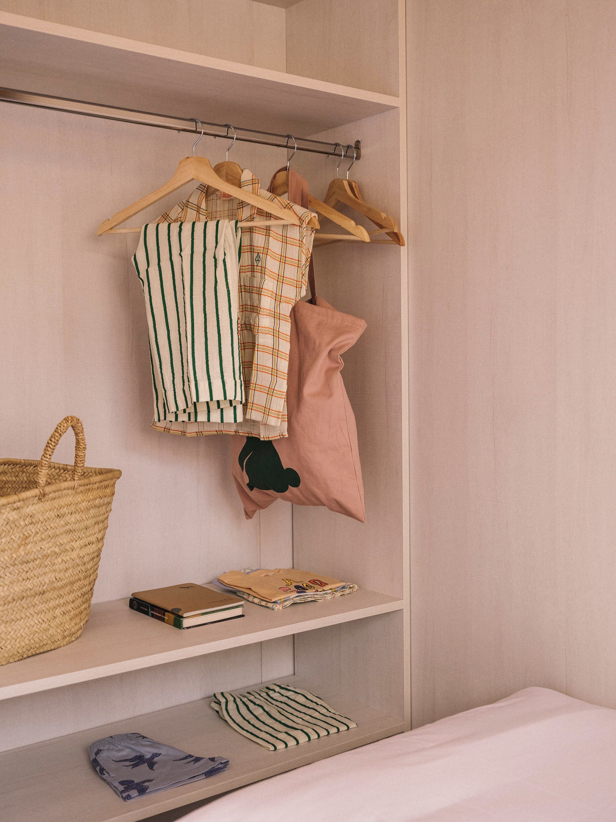 A closet with hanging clothes, a woven basket, and folded clothes on shelves.
