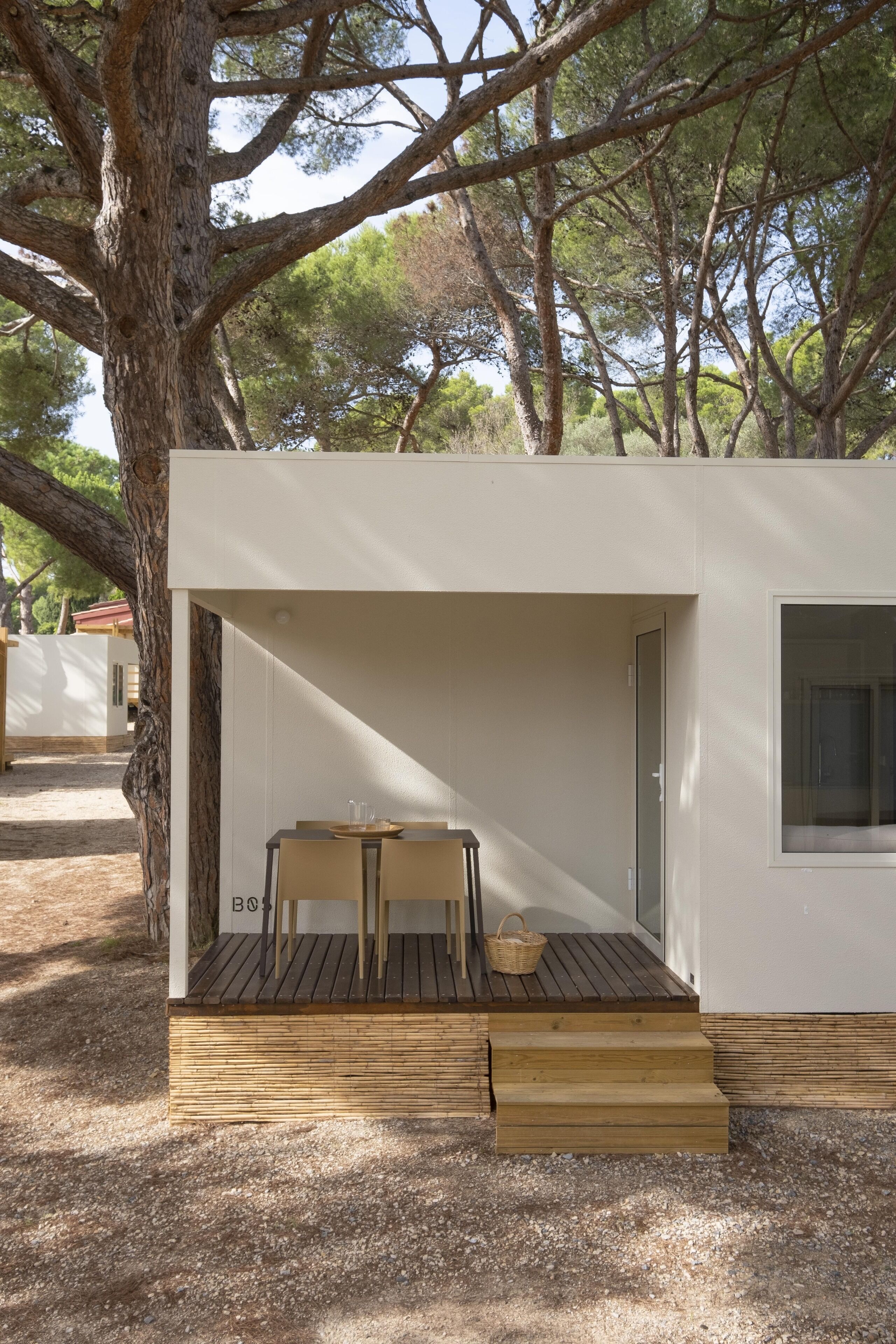 A modern, minimalist cabin with a wooden deck, a table, and a chair.