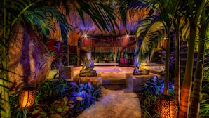 Un jardin intérieur à thème tropical, avec des allées pavées, des palmiers et un éclairage décoratif.