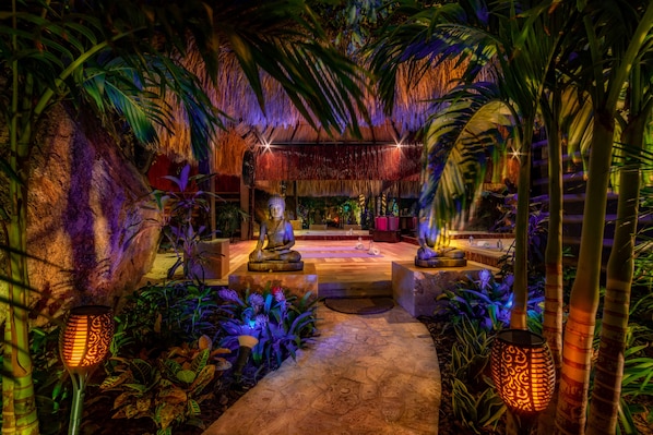 A tropical-themed indoor garden with stone pathways, palm trees, and decorative lighting.
