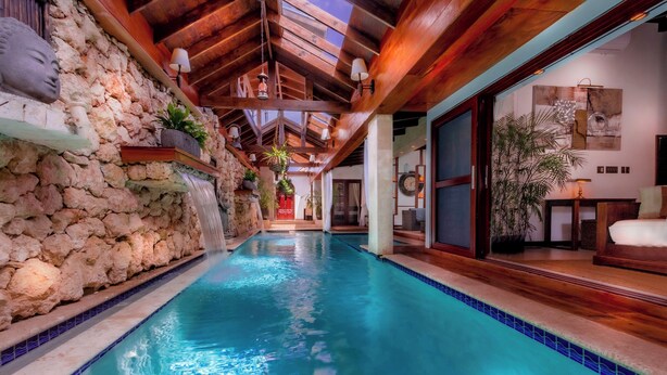 Une piscine intérieure avec un mur en pierre d’un côté et des poutres en bois au plafond.