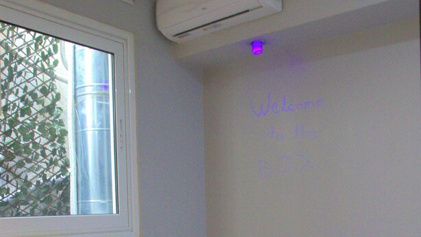 Une chambre d’hôtel avec un lit, une fenêtre, un appareil de climatisation et un mur sur lequel est inscrit un message de bienvenue.