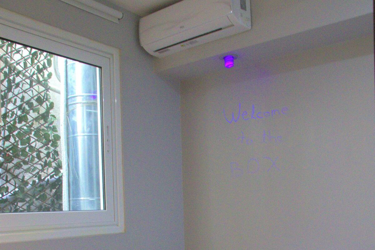 A hotel room with a bed, a window, an air conditioning unit, and a wall with a welcome message.