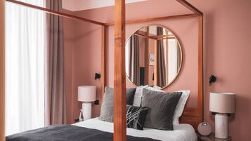 A four-poster bed with a round mirror above it, two bedside tables with lamps, and a view of the room's interior.