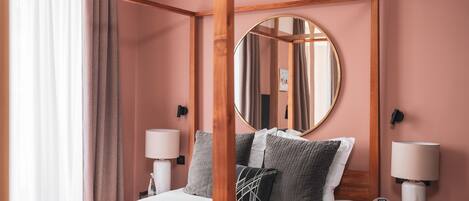 A four-poster bed with a round mirror above it, two bedside tables with lamps, and a view of the room's interior.