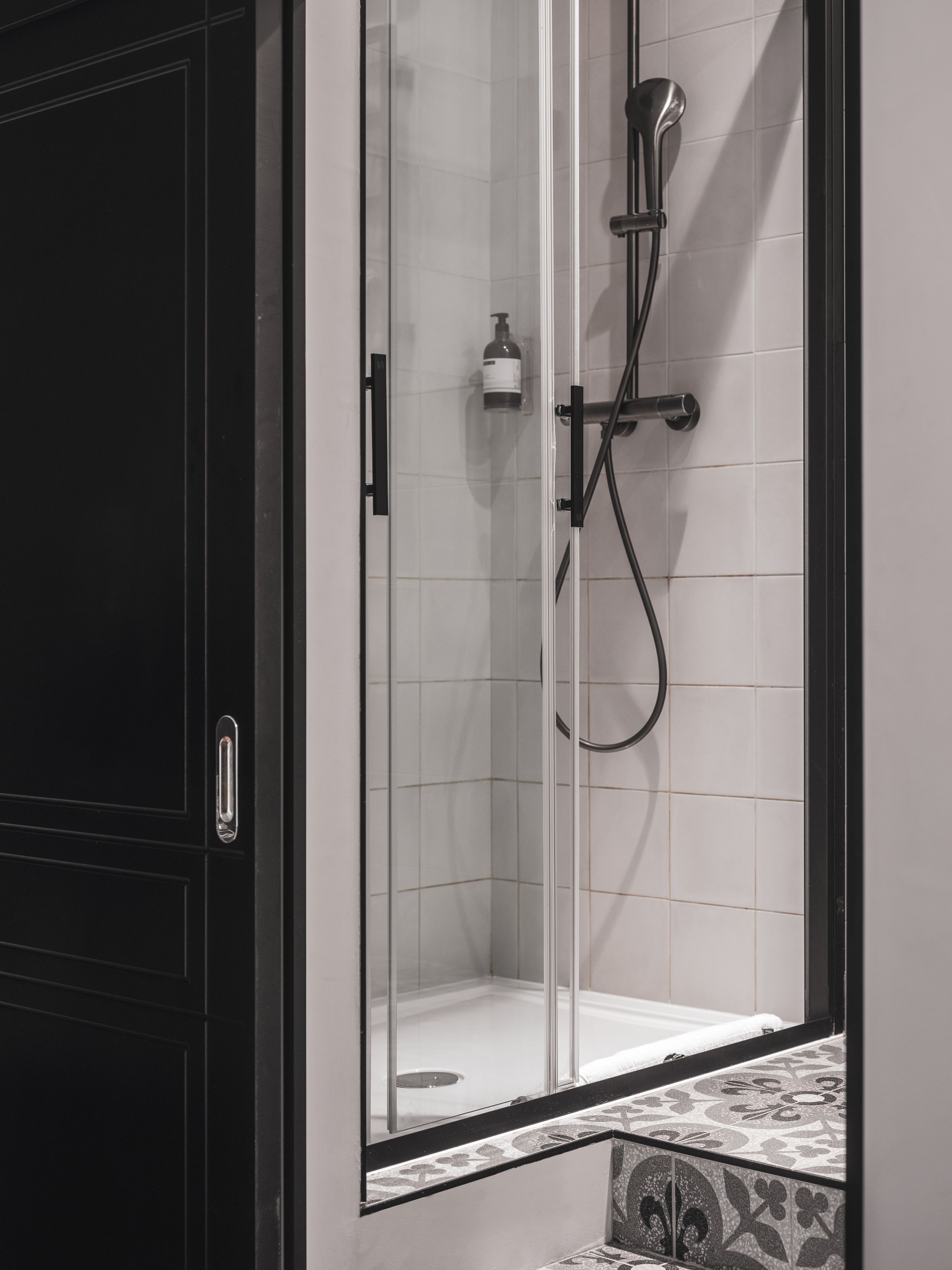 Un baño con cabina de ducha de vidrio, un cabezal de ducha manual y una botella de champú.