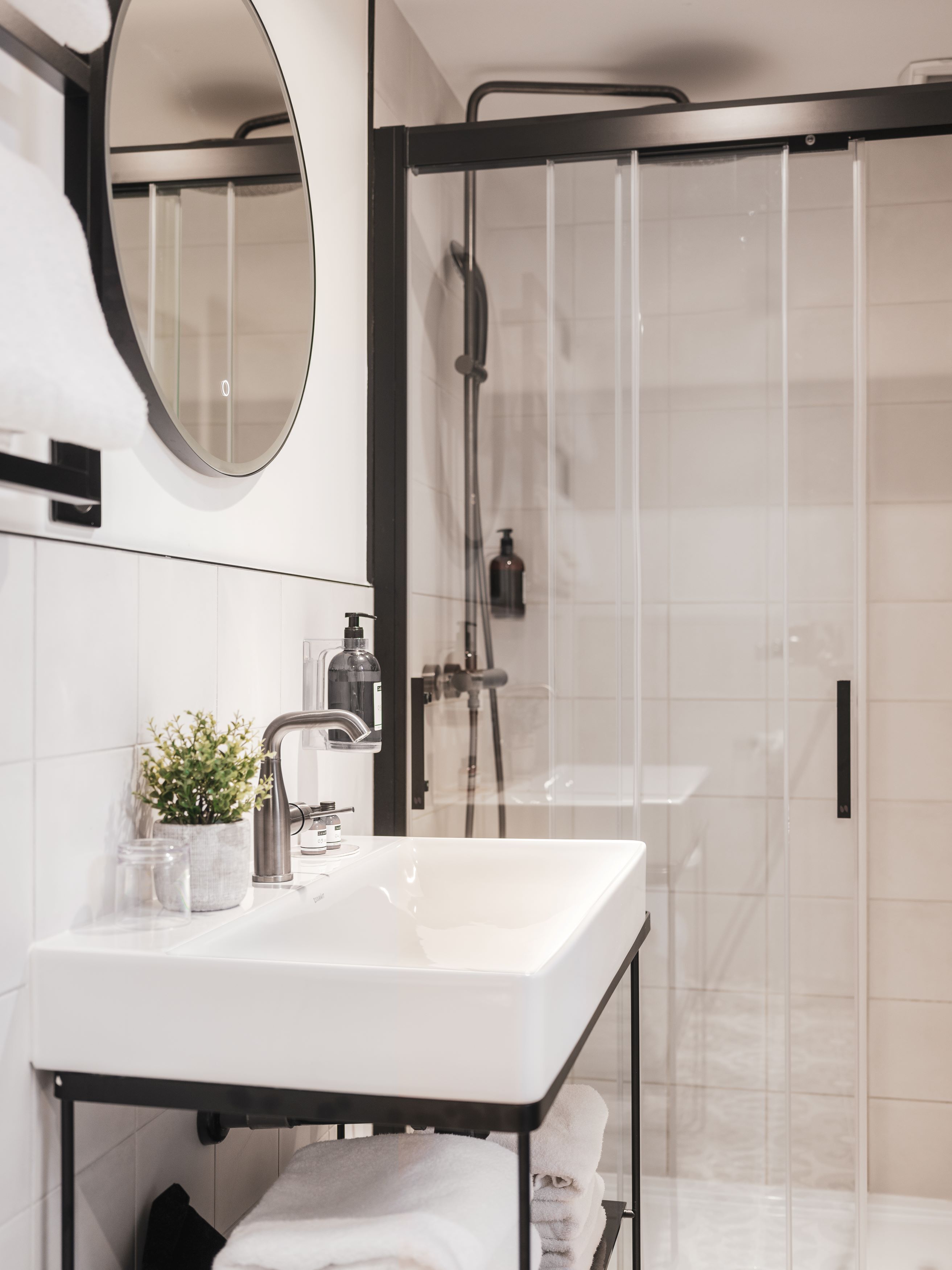 A modern bathroom with a white sink, a round mirror, and a glass-enclosed shower area.