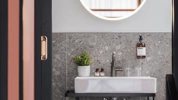 A modern bathroom with a round mirror, white sink, and a potted plant.