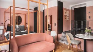 Una habitación moderna con un sofá rosa grande, una mesa de comedor con sillas, una pequeña cocina y una puerta negra.