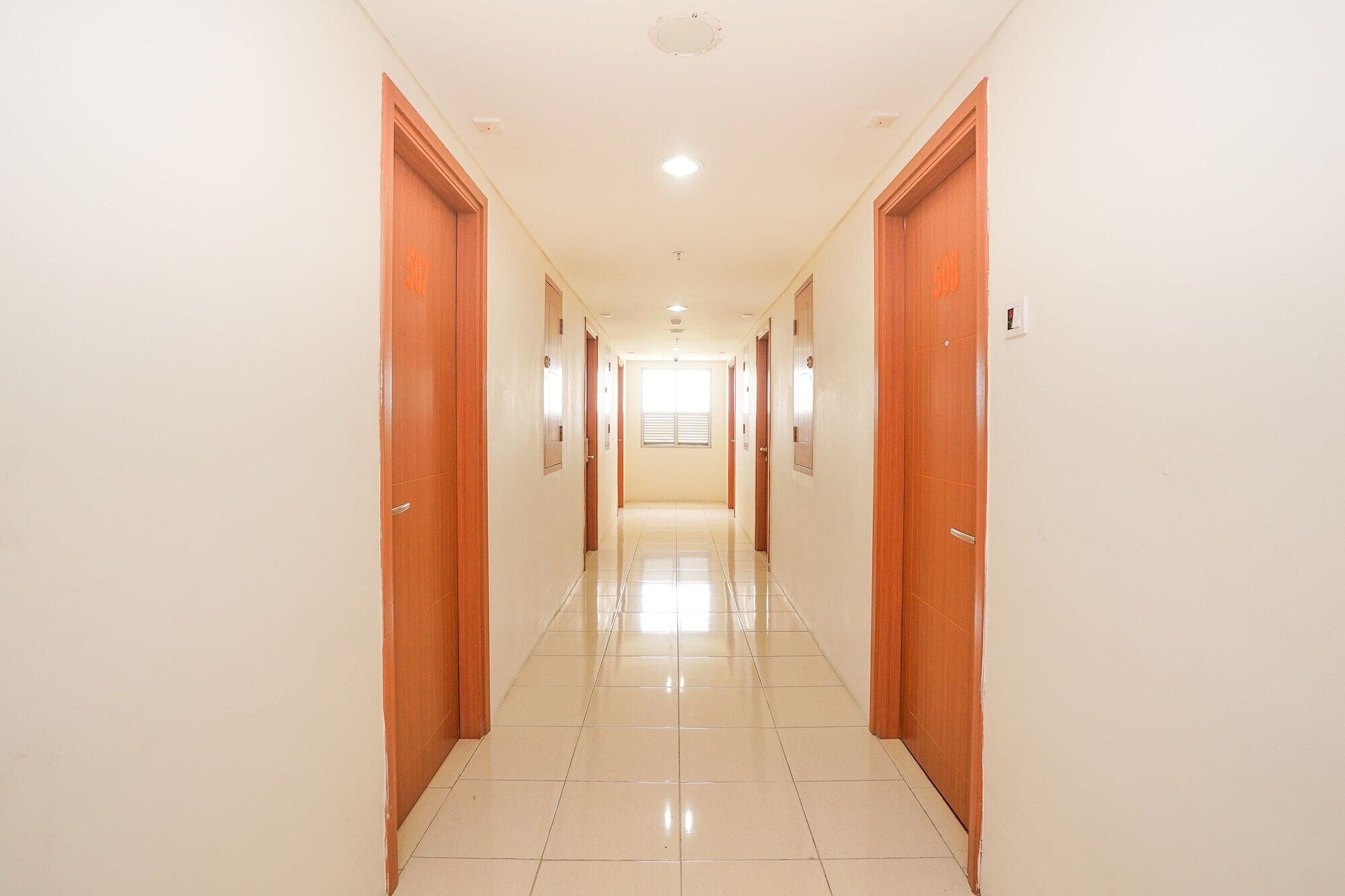 A long, narrow hallway with wooden doors on both sides, leading to a bright room at the end.
