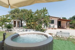 Een bubbelbad in een achtertuin met een huis, tuinmeubilair en een pergola.