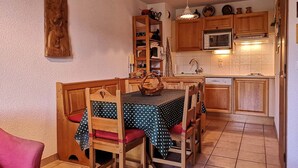 Una cocina acogedora con armarios de madera, un microondas y un lavamanos. Hay una mesa con sillas y un banco de madera.