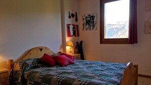 Un dormitorio acogedor con una cama de madera, una mesita de noche, una lámpara y una ventana con vistas a la montaña.