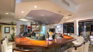 A bar area with a wooden counter, white chairs, and a stone wall. - Paphos Gardens Apartments (Paphos)