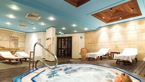 A hot tub with a person relaxing, lounge chairs, a wooden ceiling, and a tiled wall. - Paphos Gardens Apartments (Paphos)