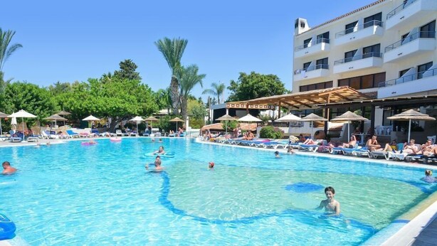 A swimming pool with lounge chairs and umbrellas, surrounded by a building with balconies. - Paphos Gardens Apartments (Paphos)