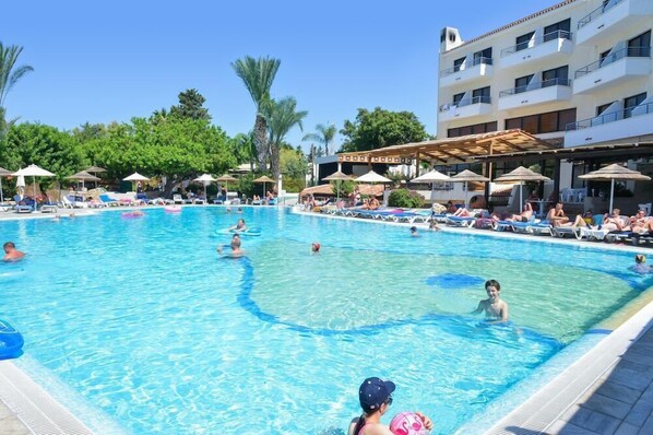 A swimming pool with lounge chairs and umbrellas, surrounded by a building with balconies. - Paphos Gardens Apartments (Paphos)