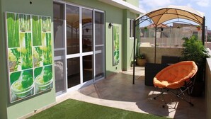 Un patio con puerta de vidrio, una silla acolchada y una zona cubierta con plantas.