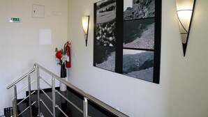 Un pasillo con una escalera, una lámpara fijada a la pared y un collage enmarcado de fotografías en blanco y negro.