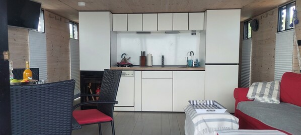 A compact kitchen with white cabinets, a small countertop, and a sink. There is a red chair and a striped sofa in the living area.