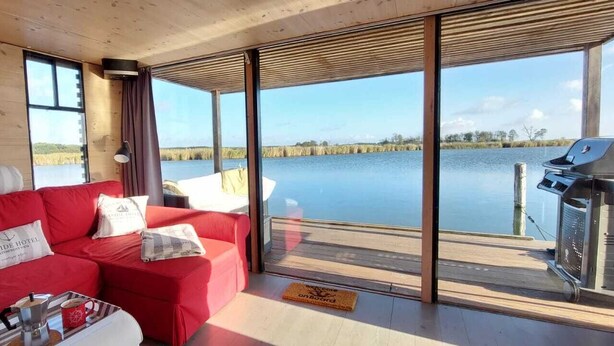Une cabane moderne avec un canapé rouge, un barbecue et une grande fenêtre donnant sur un lac.