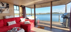 A modern cabin with a red sofa, a grill, and a large window overlooking a lake.