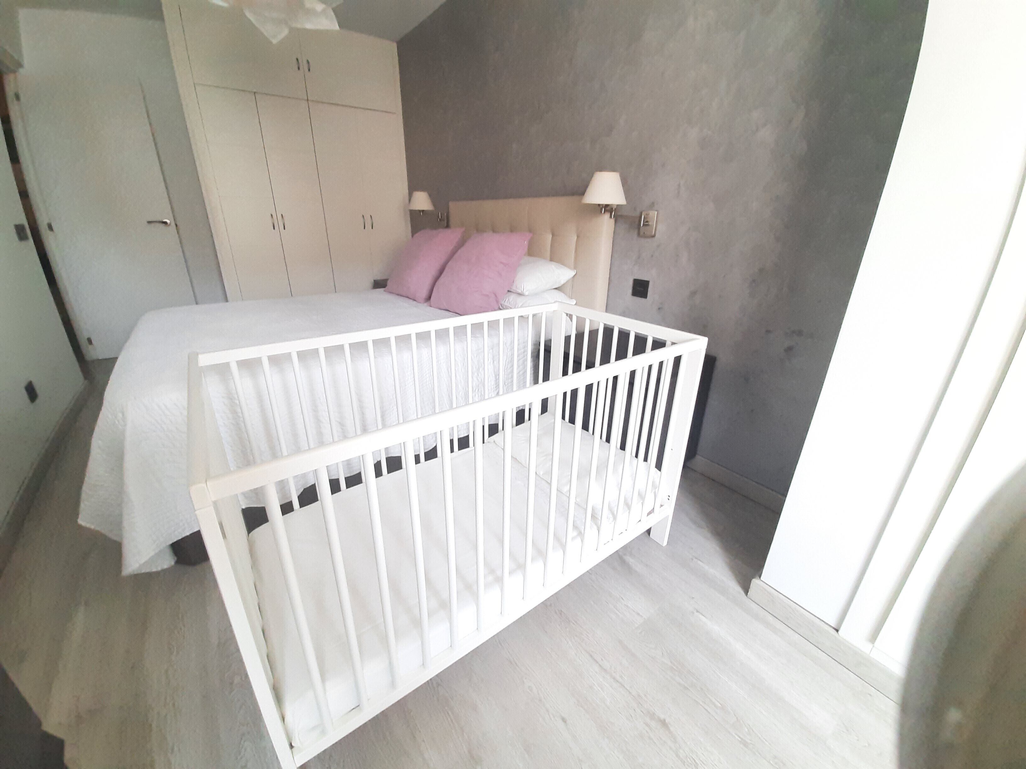 A bedroom with a bed, a crib, a wardrobe, and a lamp.