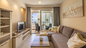 Una sala de estar moderna con sofá, mesa de centro, televisor y balcón con vista a edificios.