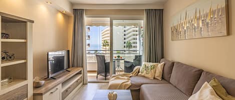 A modern living room with a sofa, a coffee table, a TV, and a balcony with a view of buildings.