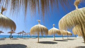Ein Strand mit reetgedeckten Sonnenschirmen und blauem Himmel.