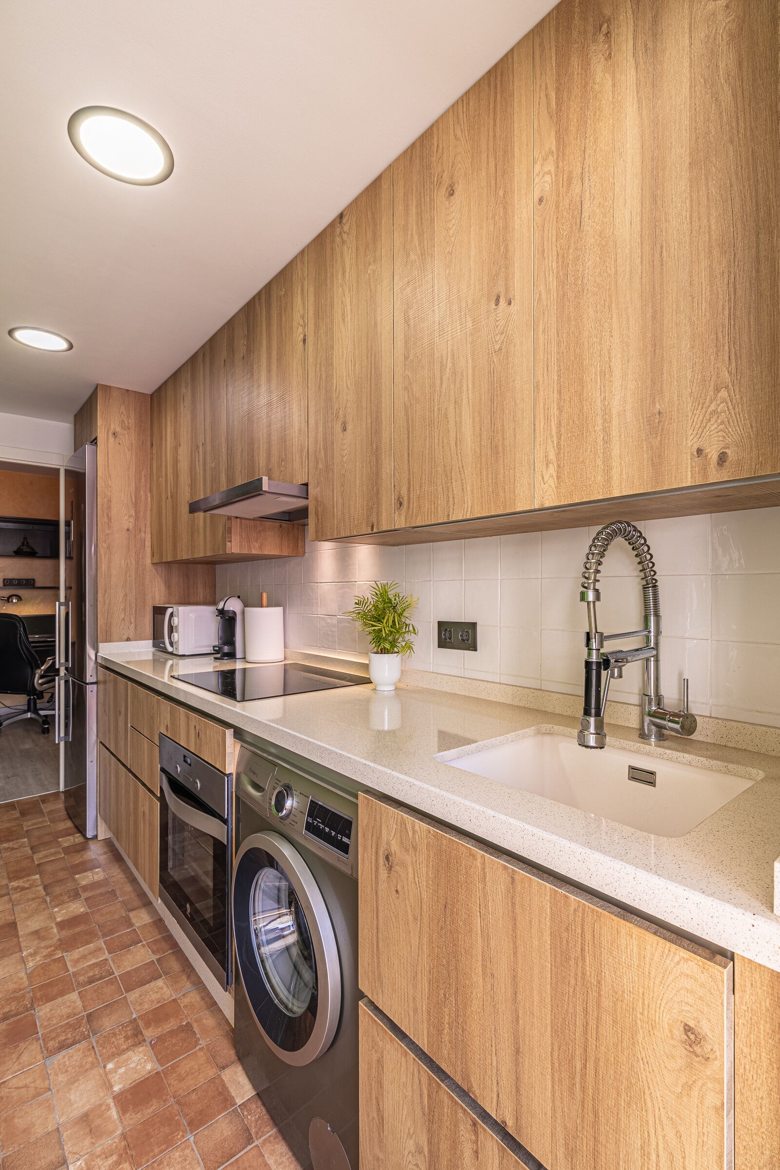 A modern kitchen with wooden cabinets, a stainless steel sink, a built-in washing machine, and a compact oven.