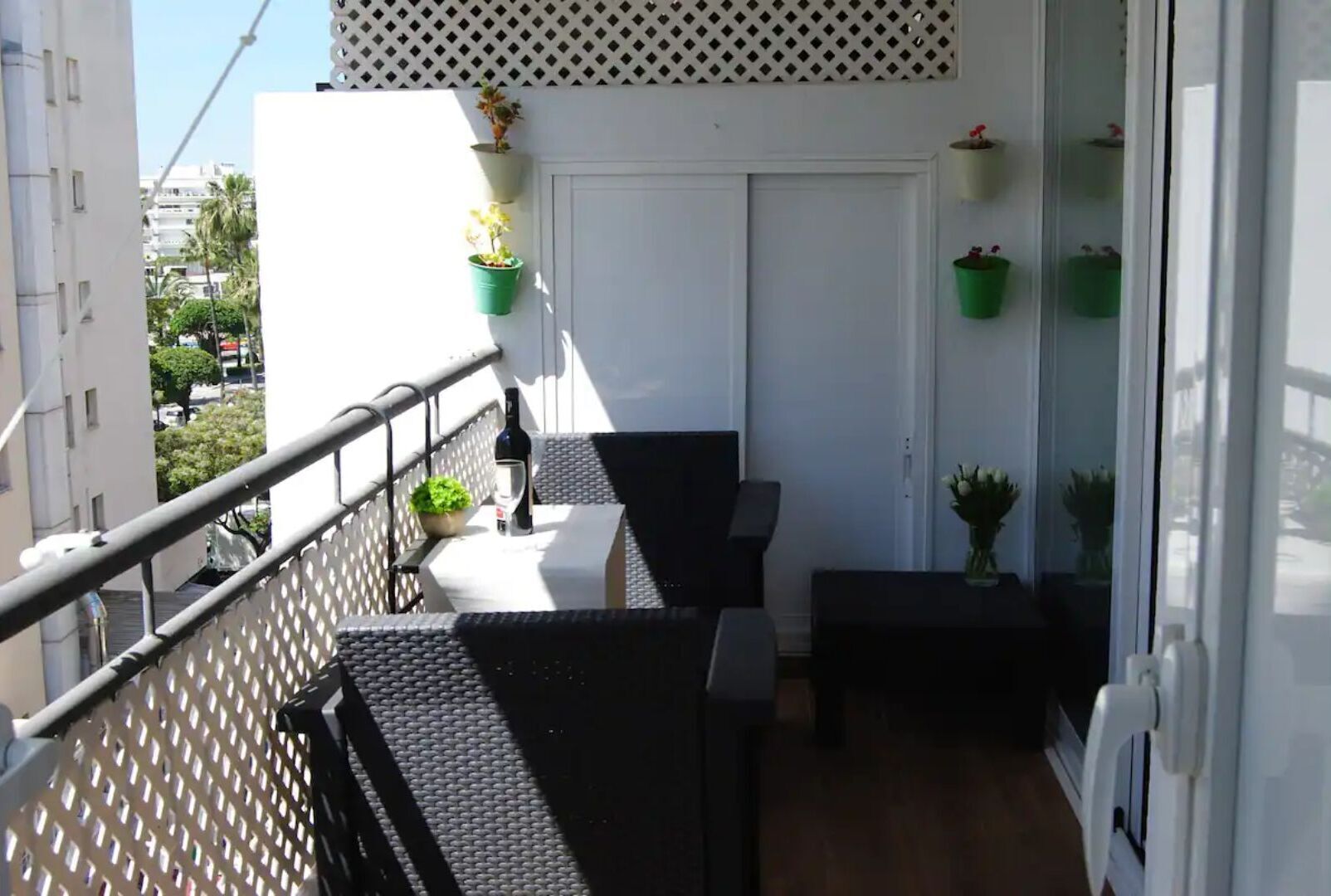 A balcony with a table and chairs, potted plants, and a bottle of wine.