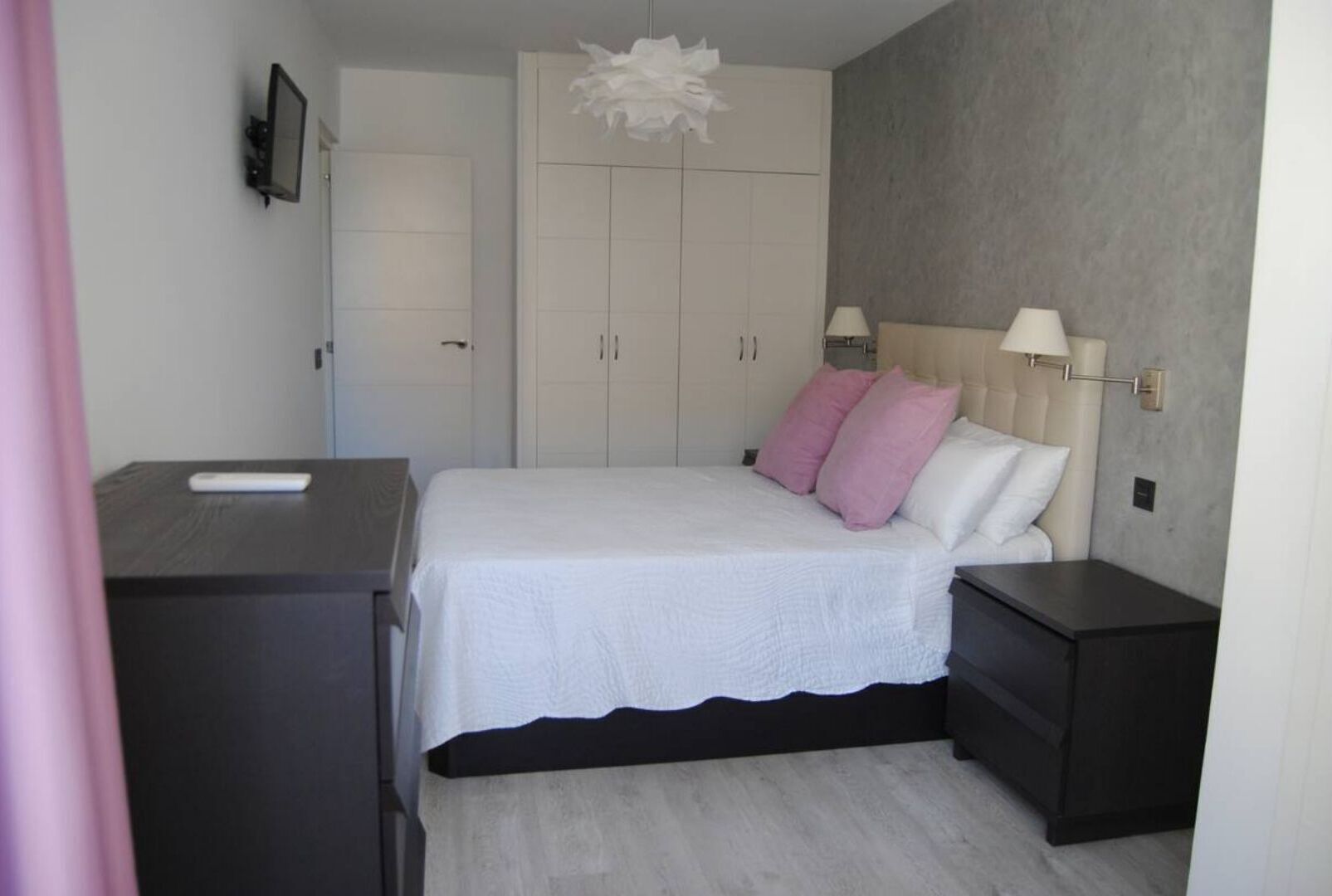 A bedroom with a bed, bedside tables, a wardrobe, and a TV on the wall.