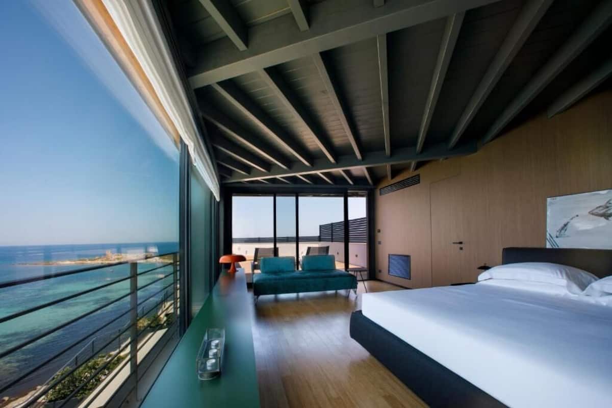 Une chambre d’hôtel moderne dotée d’un grand lit, d’un coin salon avec vue sur l’océan et d’un balcon avec une balustrade.