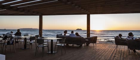 Terraza de madera con mobiliario exterior con vistas al océano al atardecer.